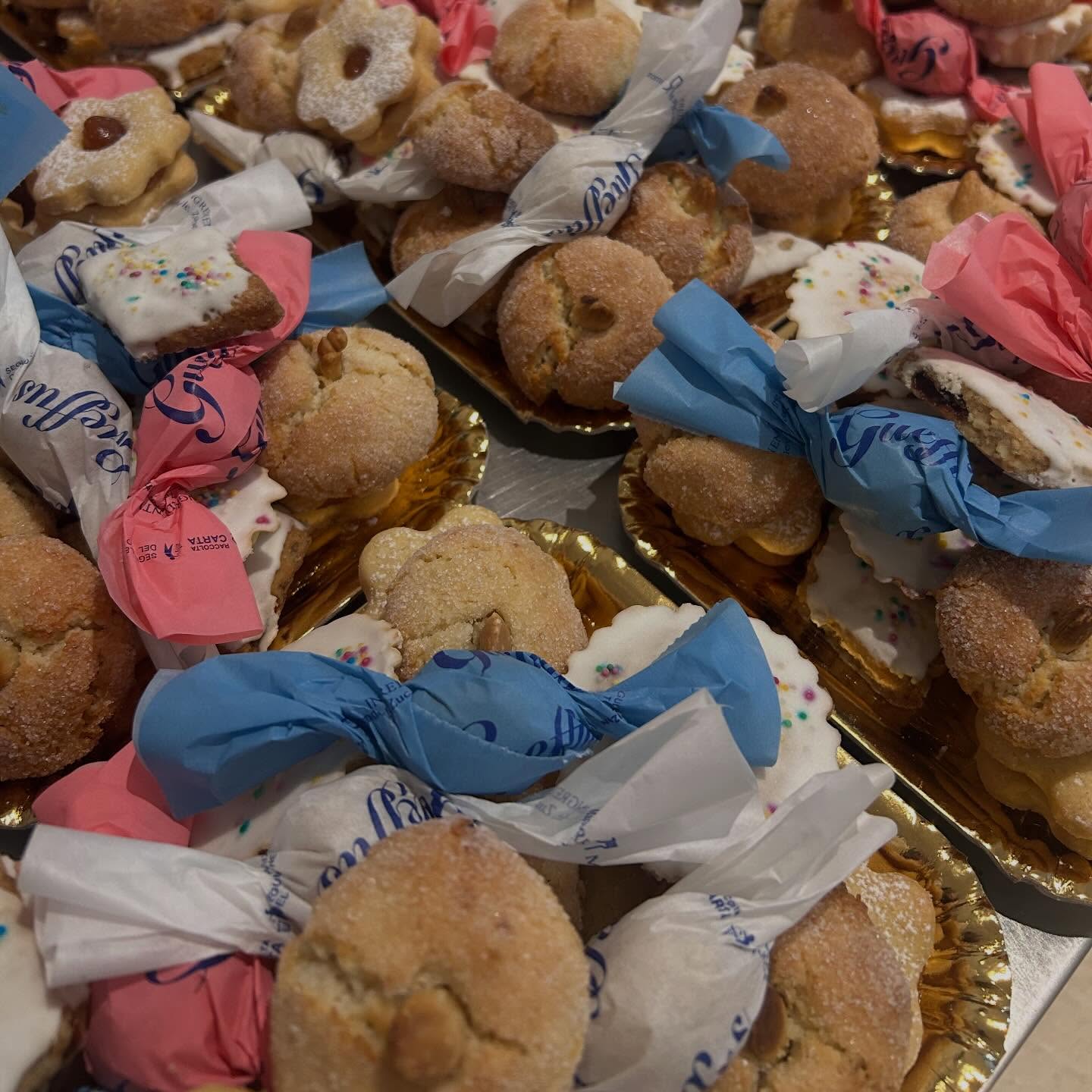 Amaretti, biscotti glassati con codette e gueffus avvolti in carta rosa, azzurra e bianca su vassoi dorati